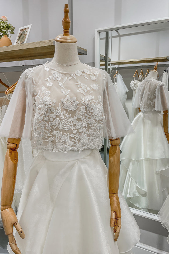 Дълга булчинска рокля Eleanor LIZA KAIN София от две части. Официална бяла рокля. Свободна горна част с високо обло деколте и ръкави от тюл. Полупрозрачна основа, покрита с флорална дантела. 