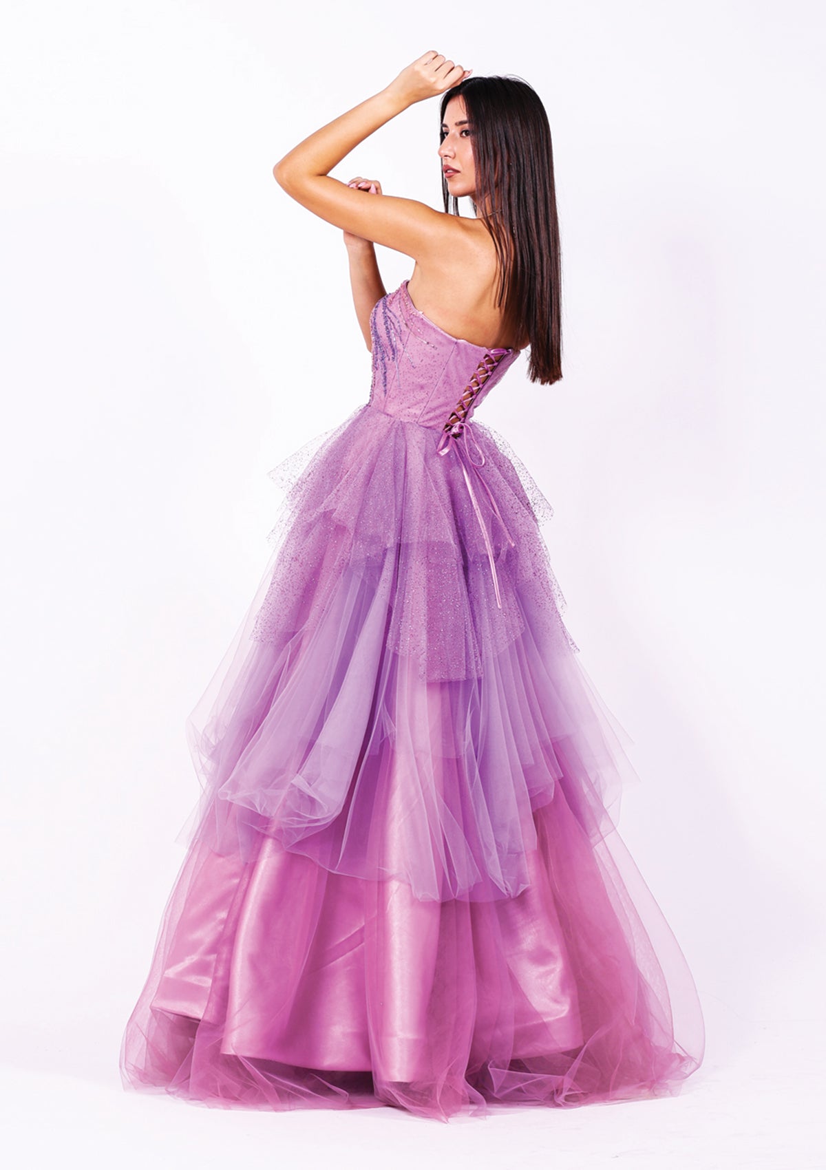 Абитуриентска рокля Ametrine LIZA KAIN София с асиметрични слоеве тюл в различни нюанси лилаво. Корсет с равно деколте и връзки на гърба. Обемна тюлена пола с волани.