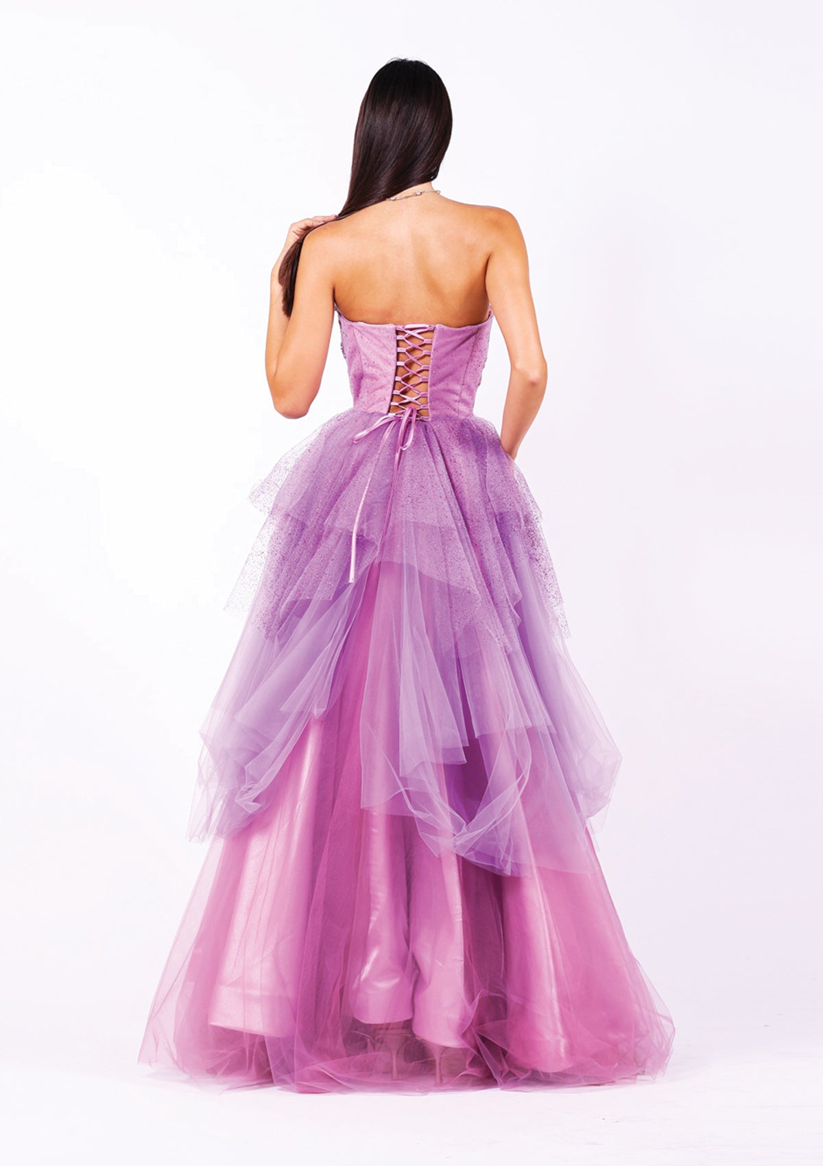 Абитуриентска рокля Ametrine LIZA KAIN София с асиметрични слоеве тюл в различни нюанси лилаво. Корсет с равно деколте без презрамки и с връзки на гърба. Бухнала пола с волани и сатенена подплата.