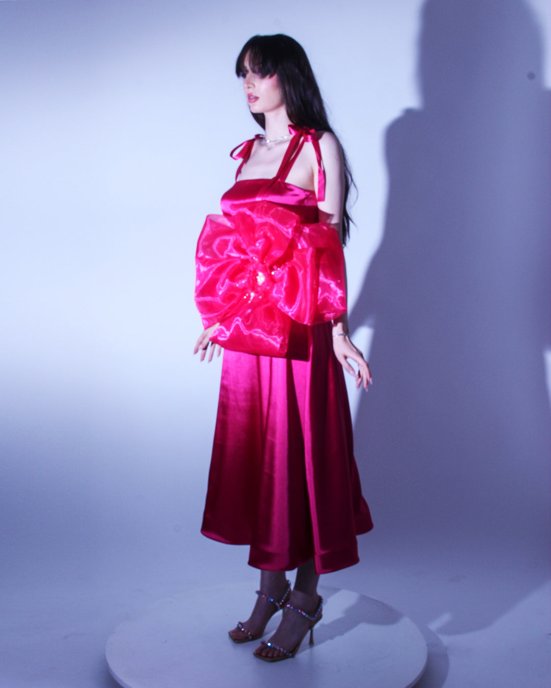 Официална рокля Aurinda LIZA KAIN София. Яркорозова сатенена рокля със средна дължина и А-линия. Корсет с равно деколте и тънки презрамки със завръзване. Голямо цвете от органза. Свободно падаща пола над глезените.