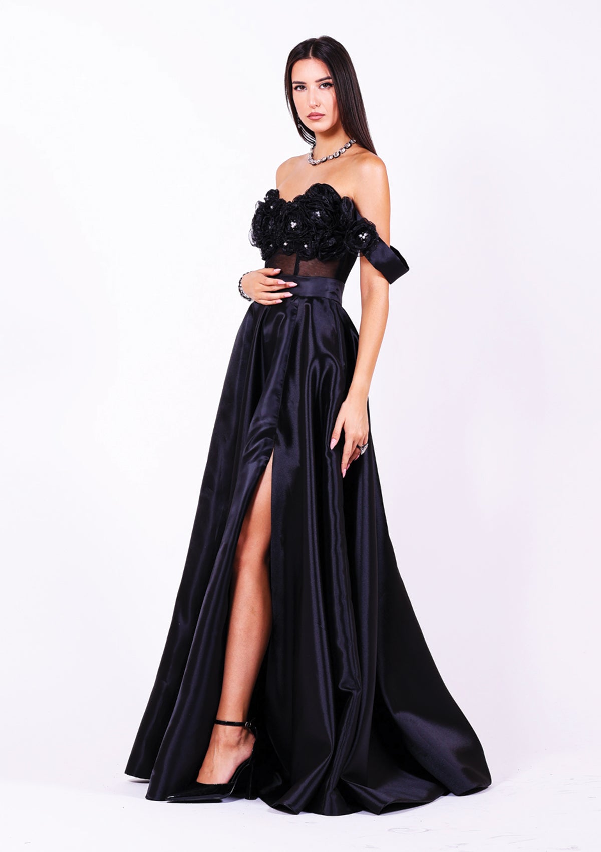 Дълга абитуриентска рокля Pearl LIZA KAIN София. Черна официална сатенена рокля от две части. Бюстие с прозрачна основа и апликации от цветя и перли. Паднали ръкави. Разкроена черна сатенена пола с широк колан, джобове и висока цепка.