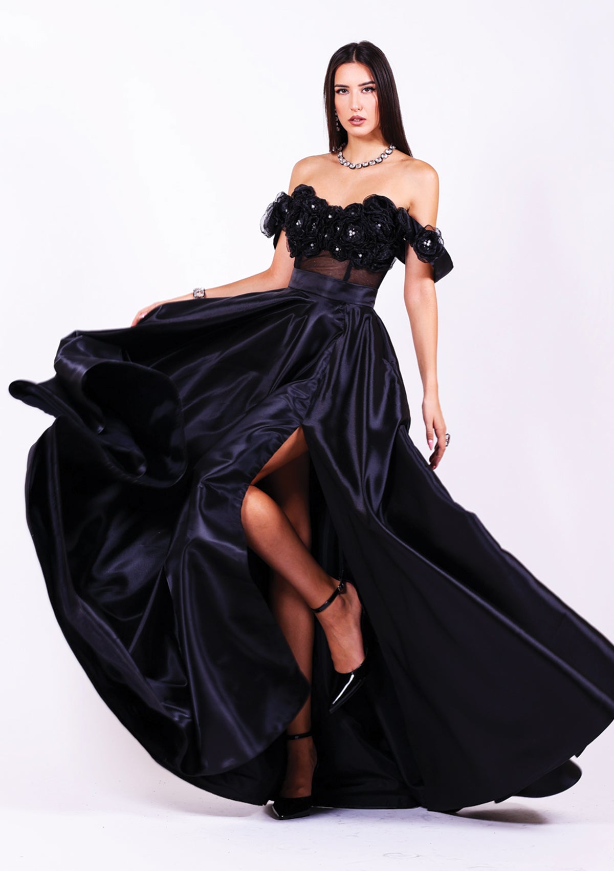 Дълга абитуриентска рокля Pearl LIZA KAIN София. Черна официална рокля от две части. Бюстие с прозрачна основа и апликации от цветя и перли. Обемна черна сатенена пола с широк колан и висока цепка.