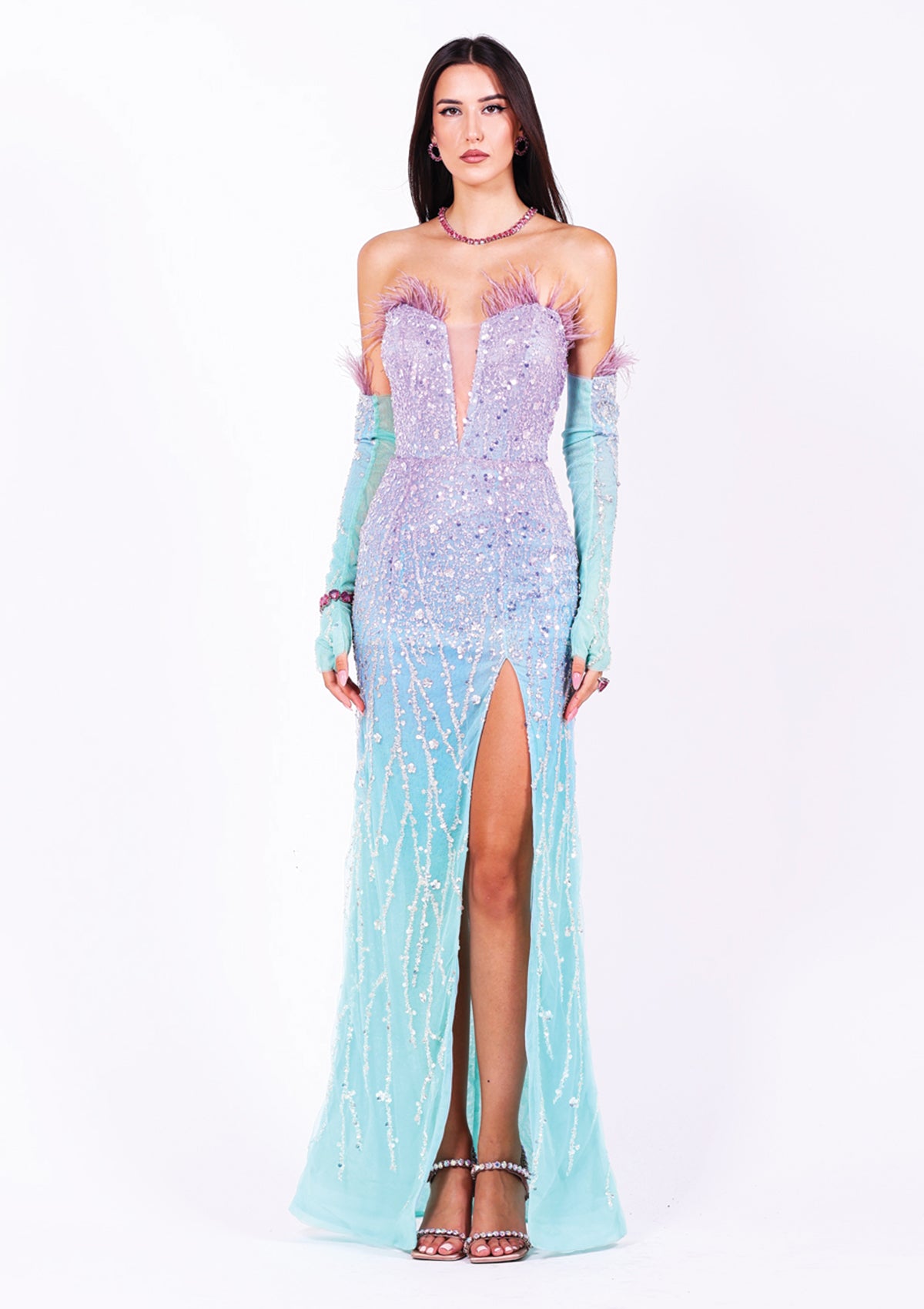 Дълга абитуриентска рокля Diaspore LIZA KAIN София. Официална рокля с кройка по тялото. Корсет без презрамки с V-образно деколте със завършек от лилави пера. Тюлена основа с преливащ ефект от лилаво към тюркоаз, покрита с пайети и бяла дантела от мъниста. Пола тип русалка с висока цепка. Ръкавици с пера.