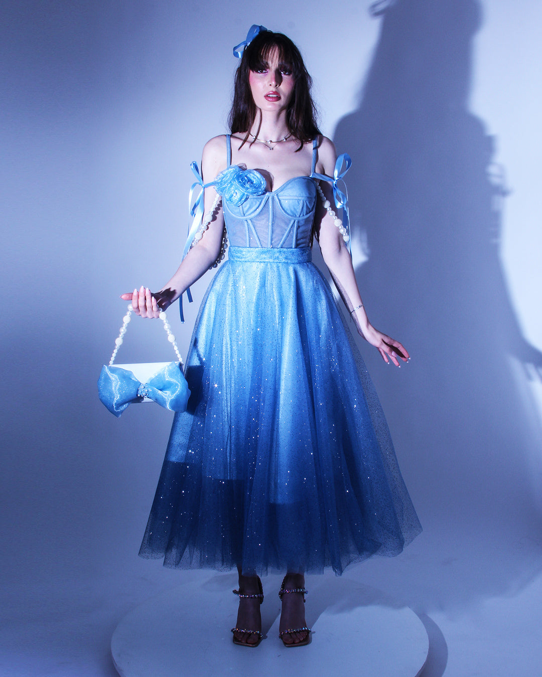 Дълга абитуриентска рокля Emmalina LIZA KAIN София. Официална рокля от син тюл. Корсет с чашки и тънки презрамки. Паднали презрамки тип панделка. Разкроена пола от блестящ тюл с подплата. Чантичка с панделка.