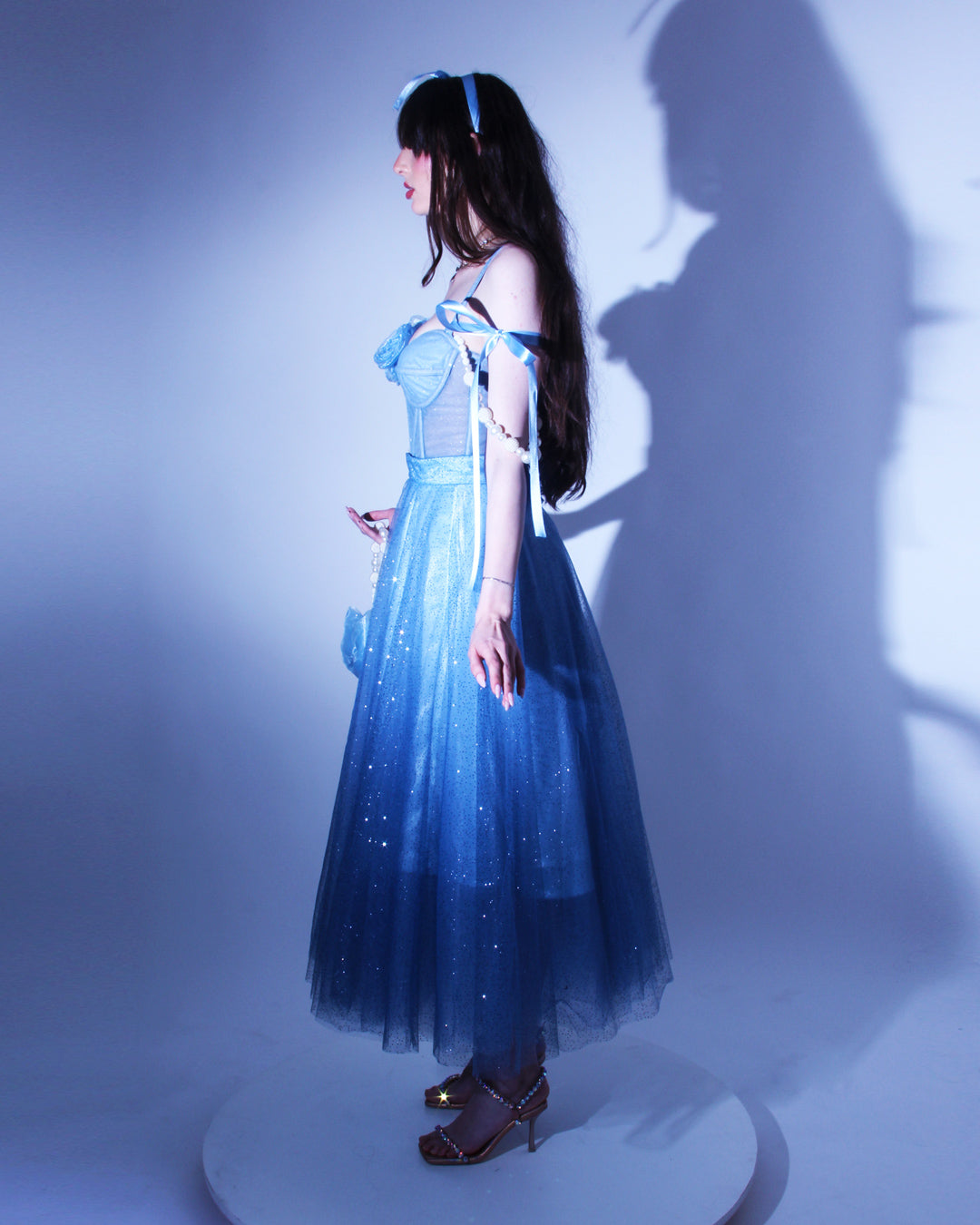 Дълга абитуриентска рокля Emmalina LIZA KAIN София. Официална рокля от син тюл. Корсет със сърцевидно деколте и тънки презрамки. Паднали презрамки тип панделка и паднали презрамки с перли. Обемна пола от блестящ тюл с подплата. Дължина до глезените.