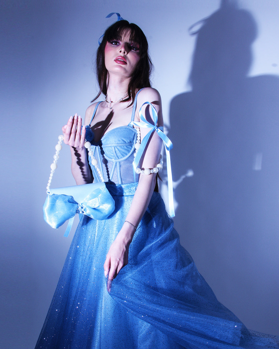 Дълга абитуриентска рокля Emmalina LIZA KAIN София. Официална рокля от син тюл. Корсет със сърцевидно деколте и тънки презрамки. Паднали презрамки тип панделка и паднали презрамки с перли. Връзки на гърба. Обемна пола от блестящ тюл с подплата. Официална чанта комплект.