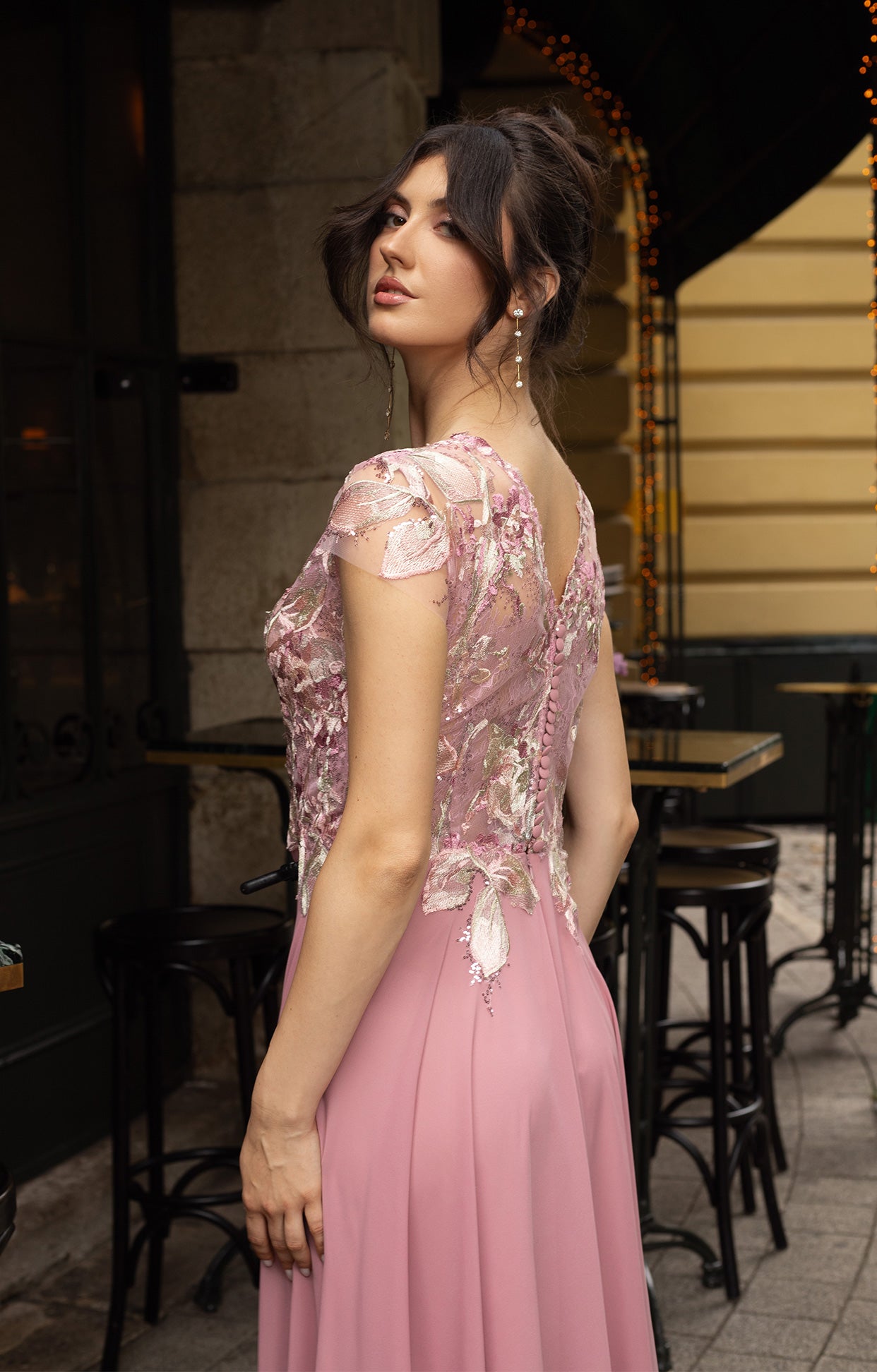 Официална дълга абитуриентска рокля Enira LIZA KAIN София. А-силует от светлорозов шифон. V-образна горна част със светлорозова памучна дантела с флорални мотиви върху прозрачна мрежа с къс ръкав. Оформяща апликация по талията. Закопчаване с облечени копчета.