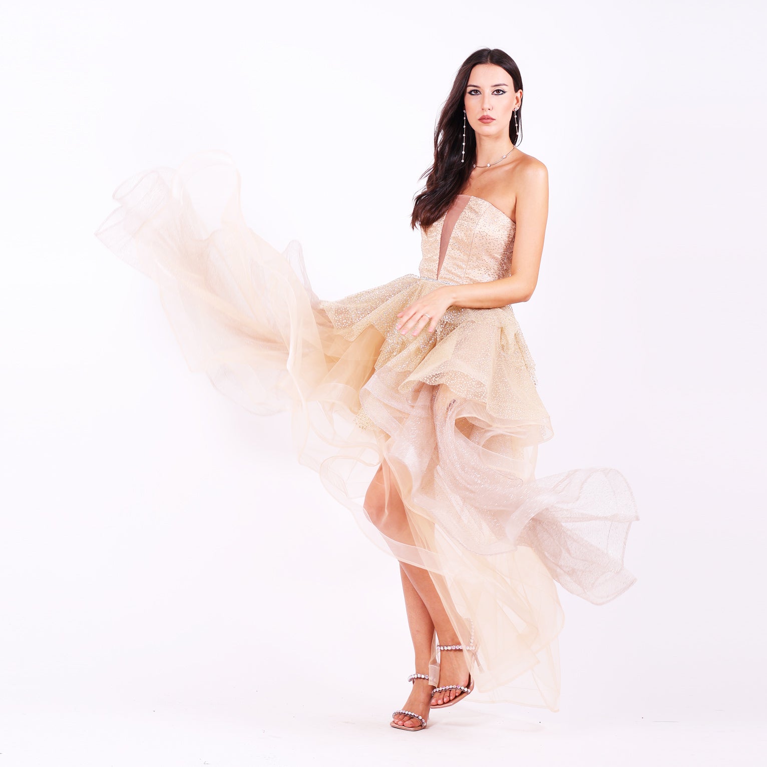 Къса абитуриентска рокля Nerium LIZA KAIN София. Официална рокля от бежов сатен и тюл. Корсет с равно деколте с мрежа, покрит със златист блестящ тюл. Клоширана обемна пола с множество къси и дълги къдрици от различни тюлове.