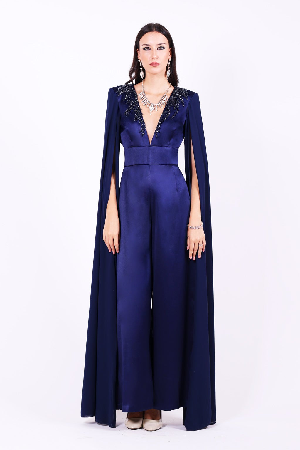 Дълъг гащеризон Iberis LIZA KAIN София. Официален гащеризон от тъмносин сатен. V-образно деколте с ръкави до земята от шифон. Апликации от графитена дантела от камъчета по деколтето. Широк колан и дълъг широк панталон.