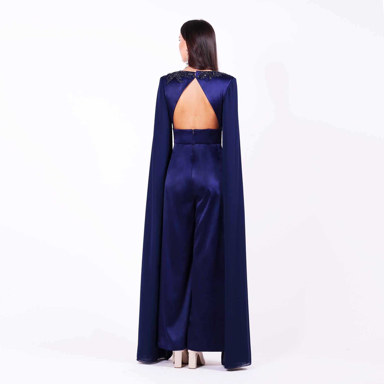 Дълъг гащеризон Iberis LIZA KAIN София. Официален гащеризон от тъмносин сатен. V-образно деколте с ръкави до земята от шифон с цепка. Отворен гръб с V форма. Широк панталон с висока талия и колан. Закопчаване с цип.