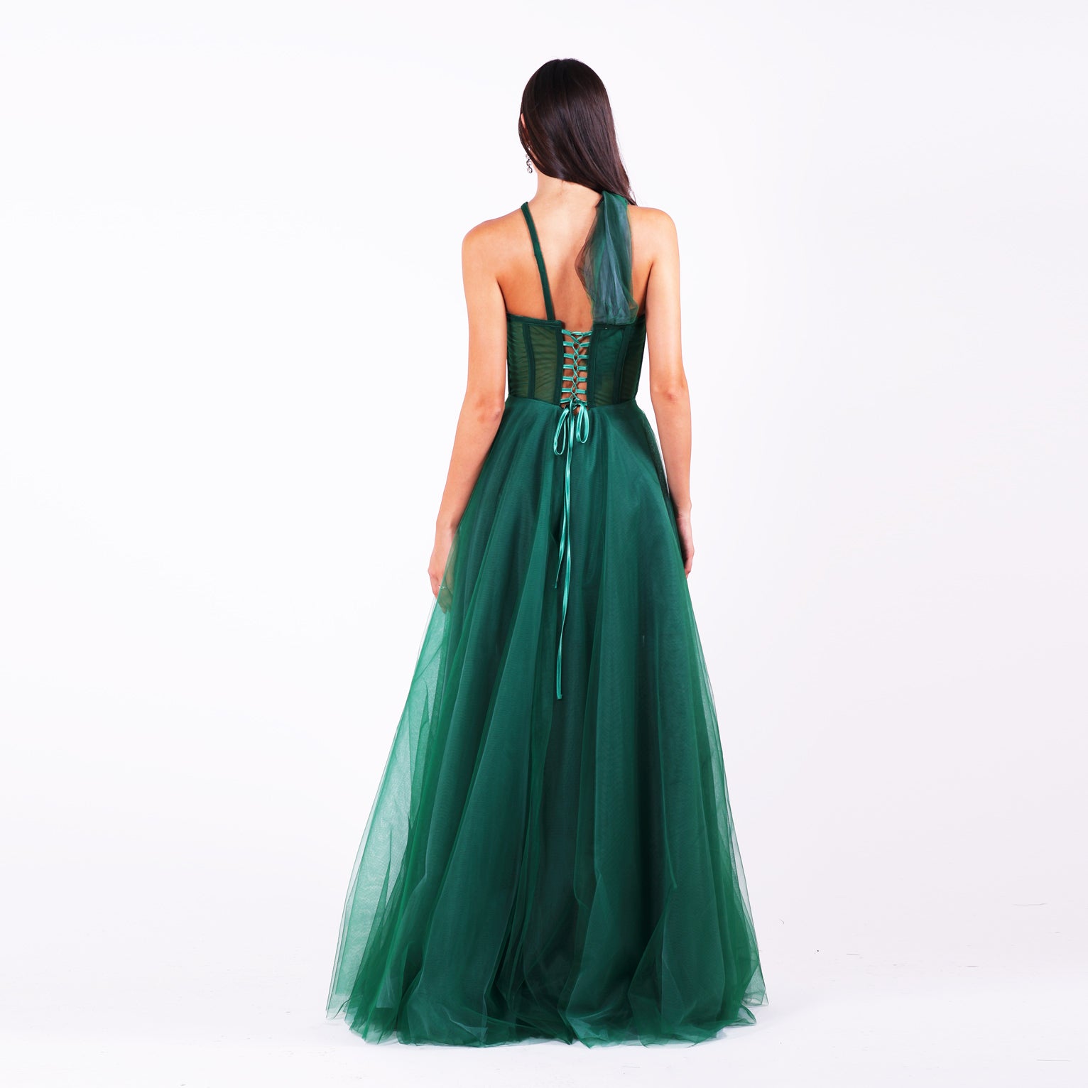 Дълга абитуриентска рокля Grevillea LIZA KAIN София. Официална рокля от тъмнозелен тюл. Корсет с полупрозрачна основа и асиметрични презрамки. Връзки на гърба. Разкроена тюлена пола от различни слоеве. 