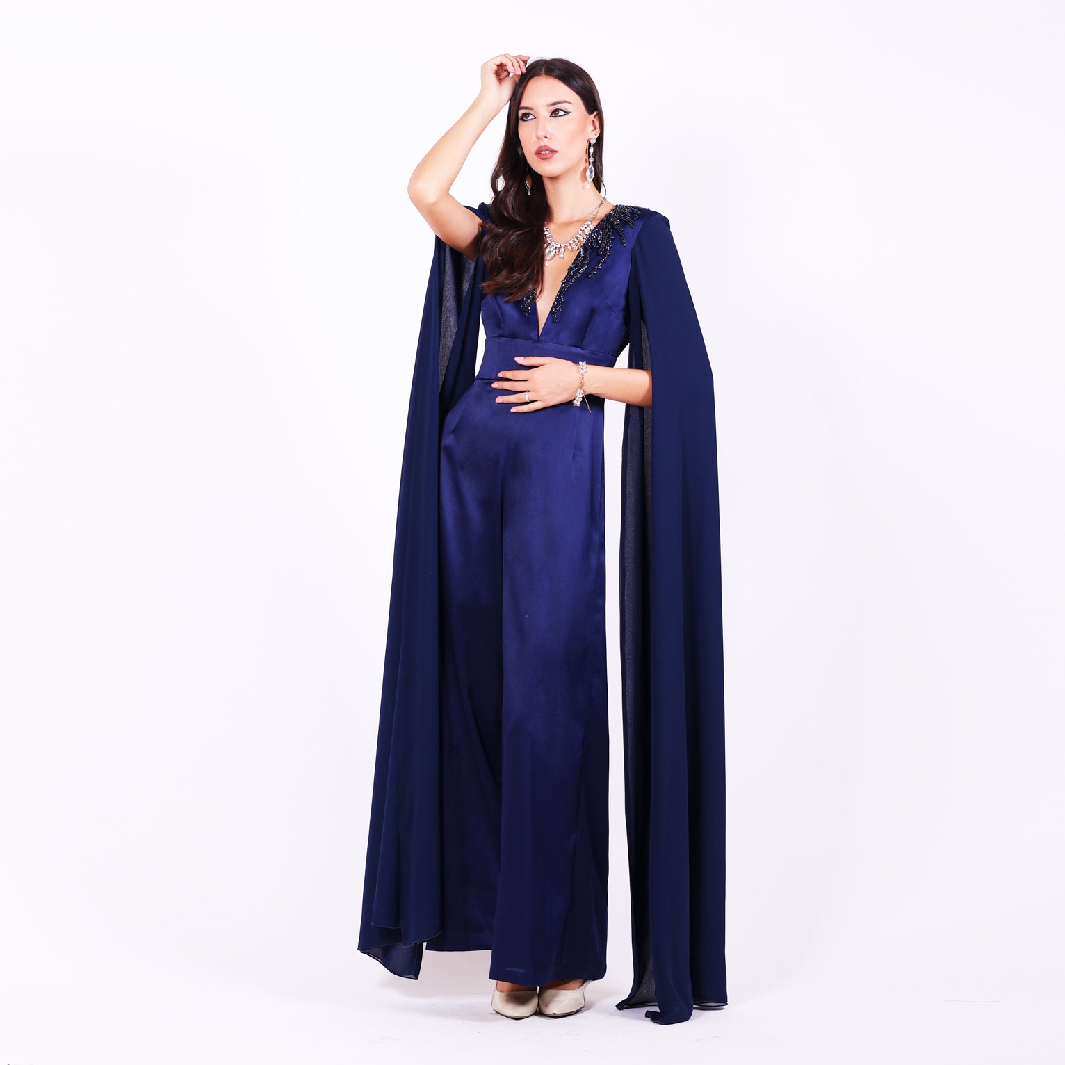 Дълъг гащеризон Iberis LIZA KAIN София. Официален гащеризон от тъмносин сатен. V-образно деколте с ръкави до земята от шифон. Апликации от графитена дантела от камъчета по деколтето. Широк колан и дълъг широк панталон.