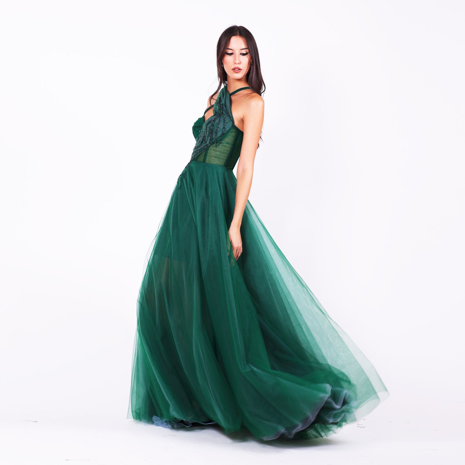 Дълга абитуриентска рокля Grevillea LIZA KAIN София. Официална тъмнозелена тюлена рокля. Корсет с полупрозрачна основа със сърцевидно деколте и асиметрични кръстосани презрамки. Обемна тюлена пола от различни слоеве. 