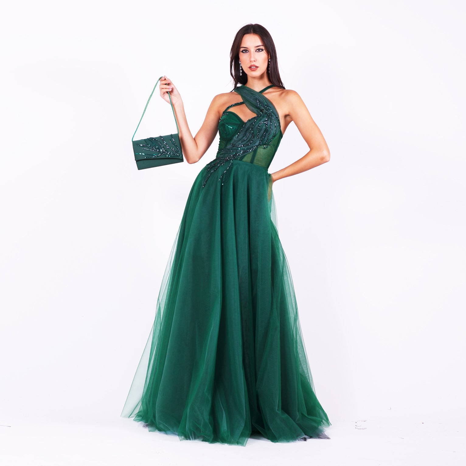 Дълга абитуриентска рокля Grevillea LIZA KAIN София. Официална рокля от тъмнозелен тюл. Корсет с полупрозрачна основа със сърцевидно деколте и апликация от тюлена драперия с дантела в кръстоска с тънка презрамка. Обемна тюлена пола от различни слоеве. Официална зелена чанта с дръжка.