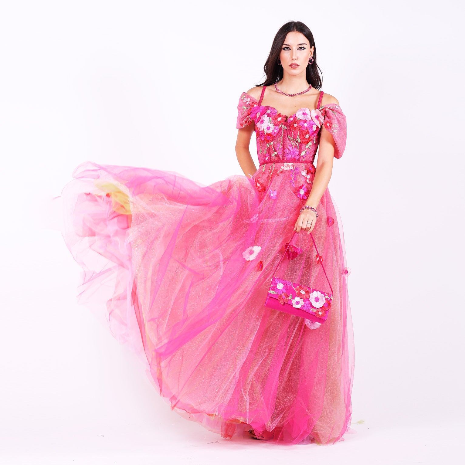 Дълга абитуриентска рокля Forsythia LIZA KAIN София. Официална рокля от яркорозов тюл. Корсет със сърцевидно деколте с тънки презрамки и паднали ръкави, покрит с дантела от памучни цветя. Бухнала тюлена пола, покрита с дантела от разноцветни памучни цветя. 