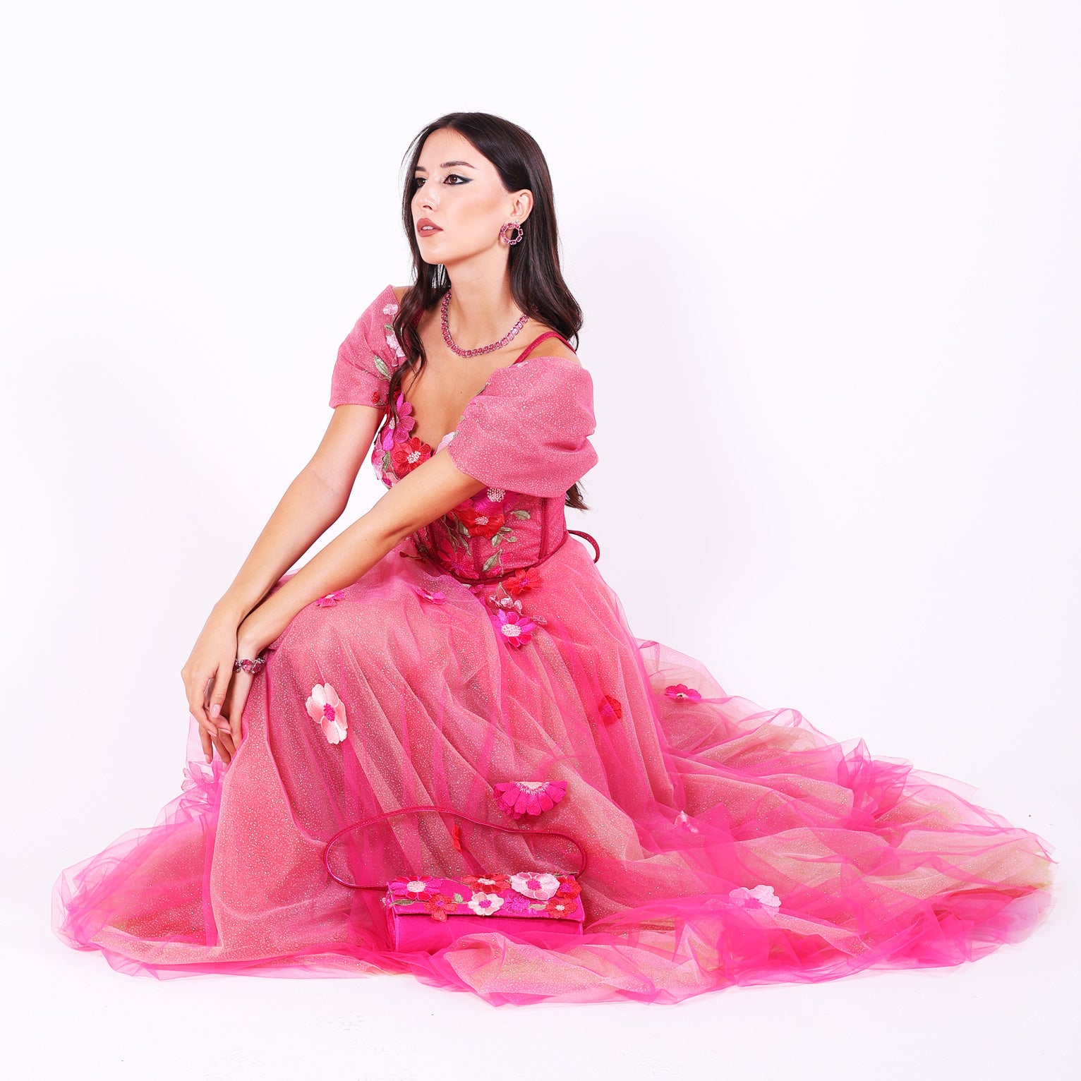 Дълга абитуриентска рокля Forsythia LIZA KAIN София. Официална рокля от яркорозов тюл. Корсет със сърцевидно деколте с тънки презрамки и обемни паднали ръкави, покрит с дантела от памучни цветя. Клоширана тюлена пола, покрита с разноцветни памучни цветя. 