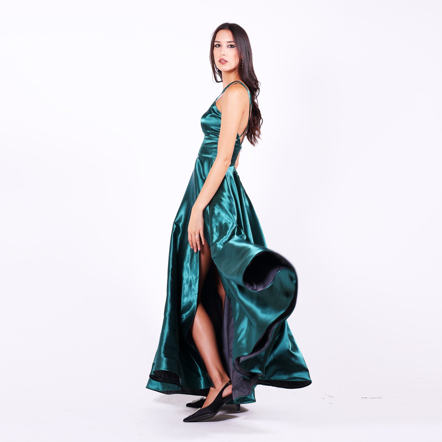 Дълга абитуриентска рокля Medinilla LIZA KAIN София. Официална рокля от петроленозелен лъскав сатен. V-образно деколте с тънки презрамки с кръстоска на гърба. Разкроена пола с широк колан и цепка.