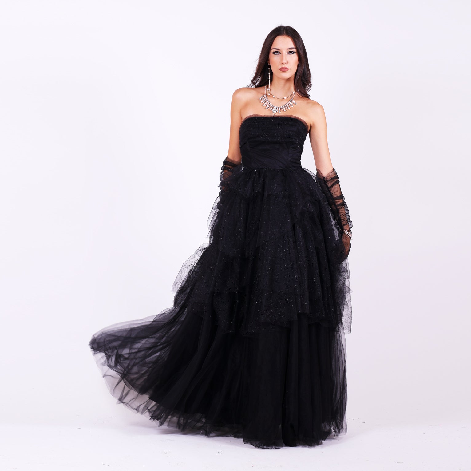 Дълга абитуриентска рокля Gloxinia LIZA KAIN София. Официална рокля от черен тюл. Корсет без презрамки с равно деколте с драперия. Разкроена пола на етажи от множество слоеве тюл. Тюлени ръкавици без пръсти.