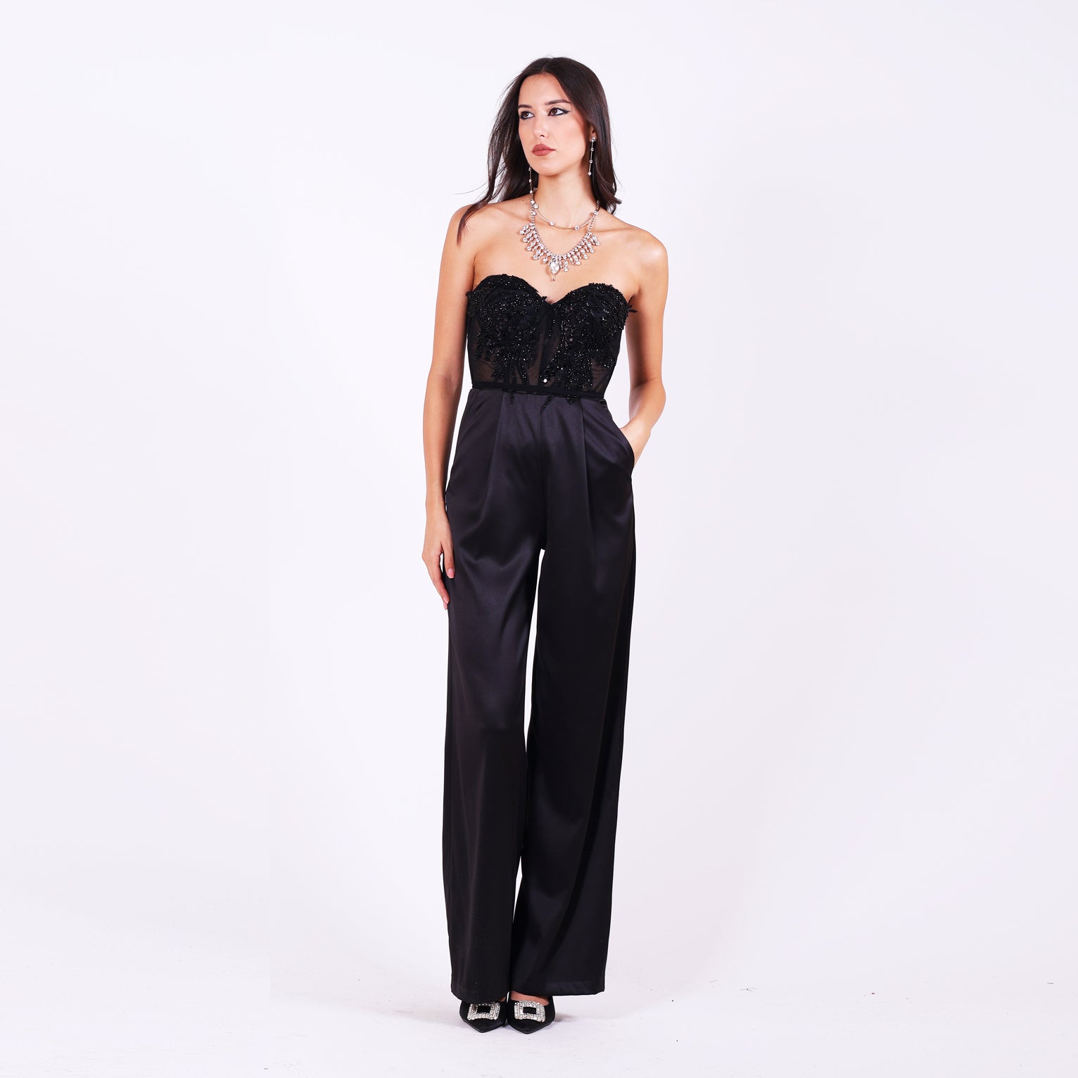 Официален гащеризон Carlina LIZA KAIN София. Черен сатенен гащеризон. Корсет без презрамки със сърчевидно деколте с полупрозрачна основа, покрита с блестяща черна дантела от мъниста и камъни. Широк сатенен панталон с плохи.