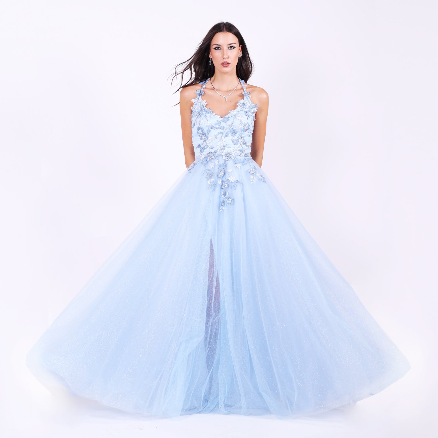 Дълга абитуриентска рокля Parrotia LIZA KAIN София. Официална рокля от светлосин тюл. V-образно деколте с презрамки, покрито с флорална памучна дантела. Бухнала тюлена пола с флорални апликации по талията.