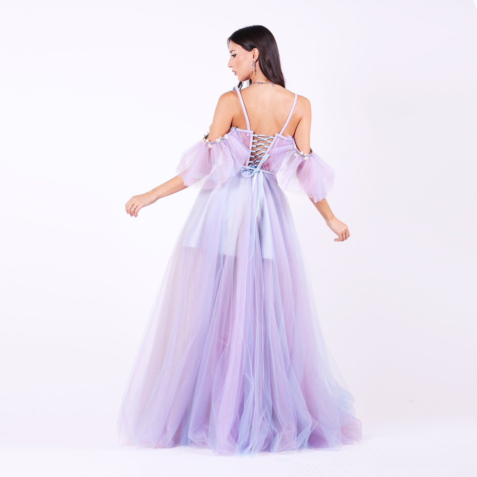 Дълга абитуриентска рокля Faucaria LIZA KAIN София. Официална рокля от светлолилав тюл с обемна кройка. Корсет със сърцевидно деколте с тънки презрамки и паднали ръкави. Връзки на гърба. Бухнала пола от множество слоеве тюл с къса сатенена подплата.