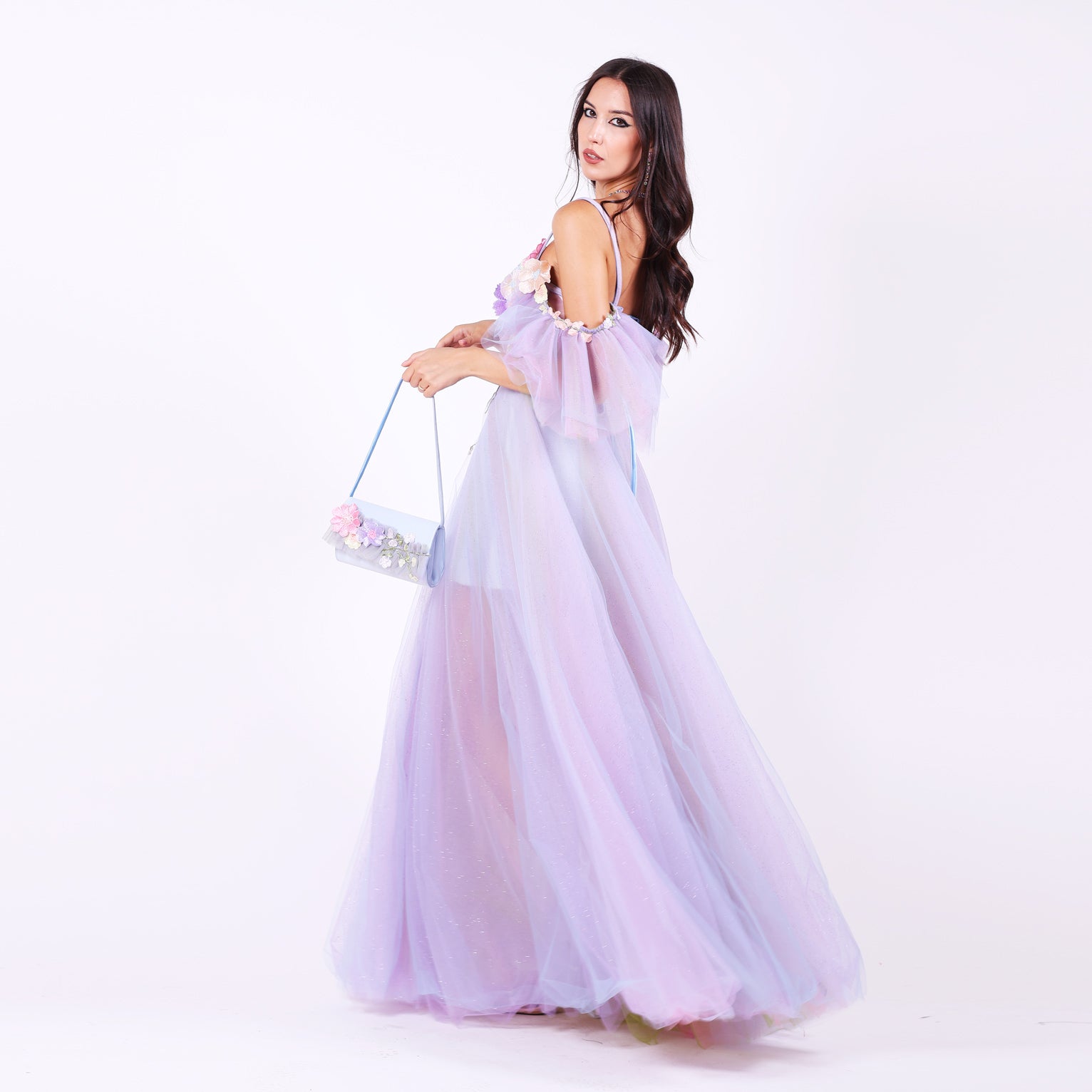 Дълга абитуриентска рокля Faucaria LIZA KAIN София. Официална рокля от светлолилав тюл. Корсет със сърцевидно деколте с тънки презрамки и паднали ръкави от тюл.  Апликации от цветя. Обемна пола от множество слоеве тюл с къса сатенена подплата. Официална чанта като роклята.