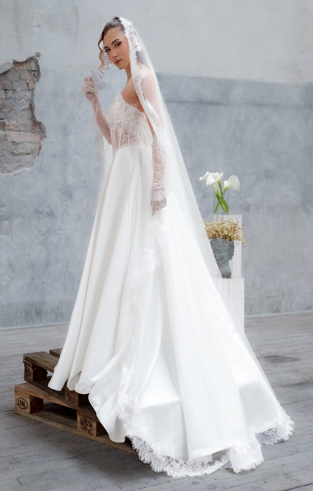 Булчинска рокля Juliette Royale LIZA KAIN Bridal с лодкообразно деколте, издължен корсет с триъгълна линия, флорална дантела и сатенена пола с обемни плохи.