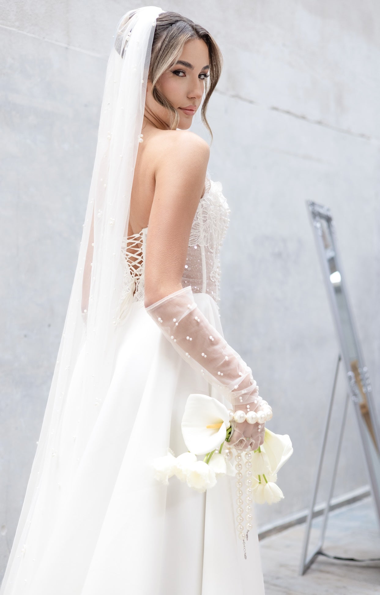 Булчинска рокля Emeralda Boheme LIZA KAIN с асиметрично деколте, прозрачна флорална дантела и ръчно нашити перли. Бяла сатенена пола с шлейф.