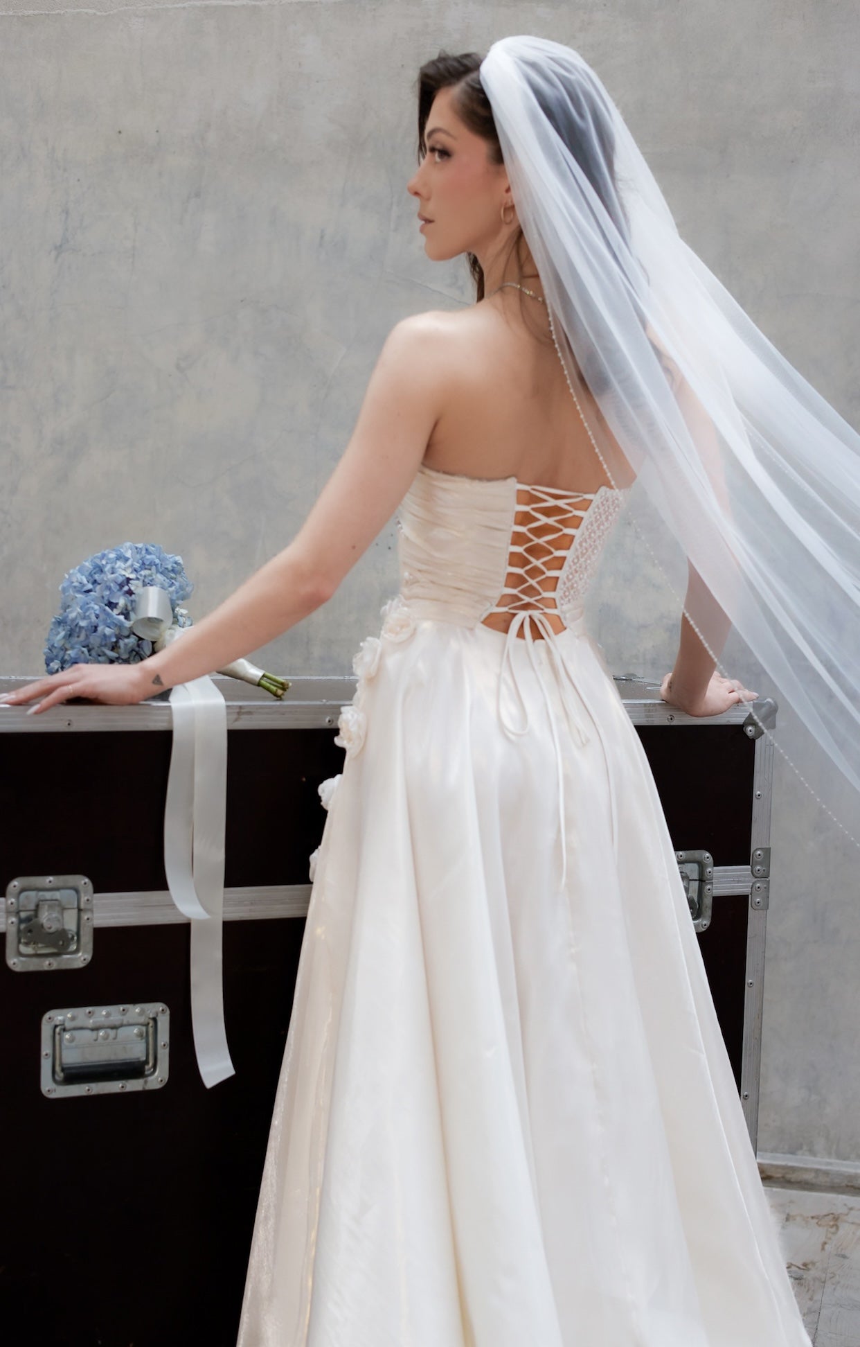 Официална булчинска рокля Moonblush LIZA KAIN Bridal с корсетирана горна част, полупрозрачна талия с нашита дантела, закопчаване с връзки. Пола от бяла органза с флорални елементи.