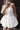 Модерна къса булчинска рокля Isolde Blanche LIZA KAIN Bridal с корсетирана горна част за придаване на женствен силует, отворено деколте с ушички, декорации от кристалчета и кристална панделка и къса балон пола от сатен.