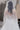 Зашеметяваща булчинска рокля Cordelia Grace от LIZA KAIN bridal с дълбок гол гръб и елегантна издължена линия. Моделът е допълнен от дълъг сватбен воал, обсипан с перли, и фини дантелени ръкавици.