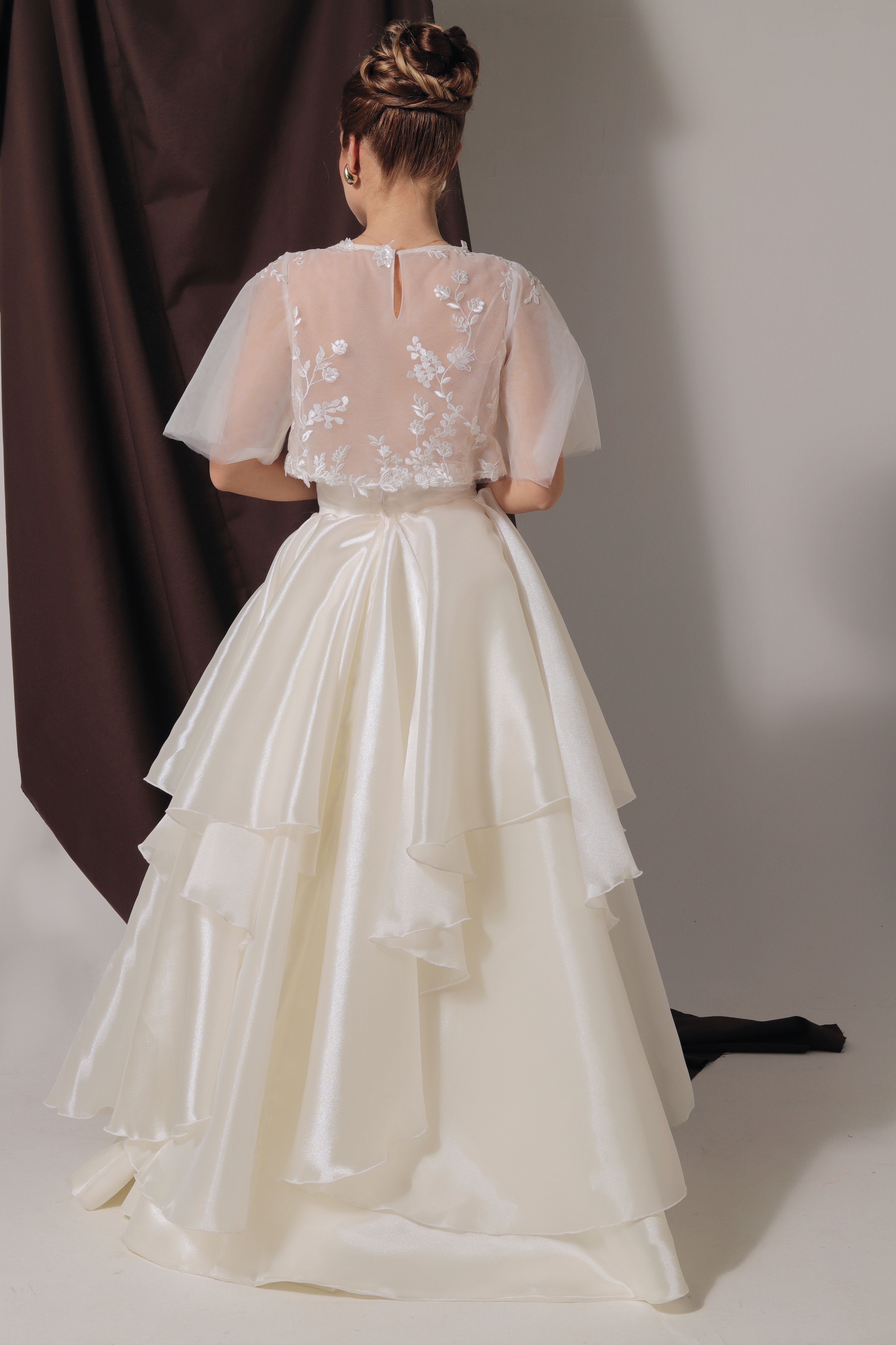 Дълга булчинска рокля Eleanor LIZA KAIN София от две части. Официална бяла рокля. Свободна горна част с ръкави от тюл. Закопчаване с копче. Прозрачна основа, покрита с флорална дантела и детайли по гърба. Пола от органза с колан и воали. 