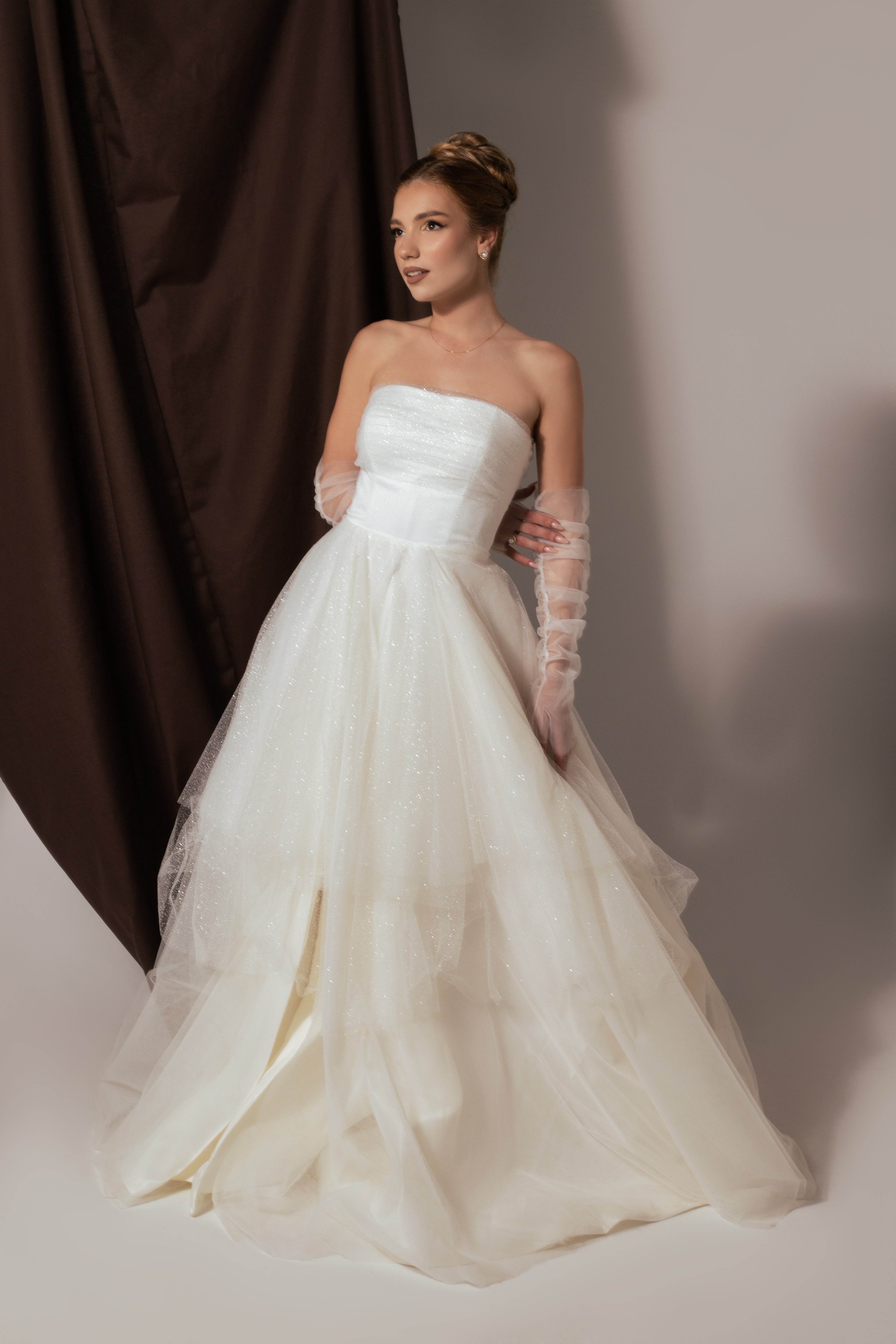 Дълга булчинска рокля Nerissa LIZA KAIN София. Бяла официална рокля от тюл. Корсет с равно деколте с драперия. Бухнала пола от множество слоеве бял тюл. Тюлени ръкавици.