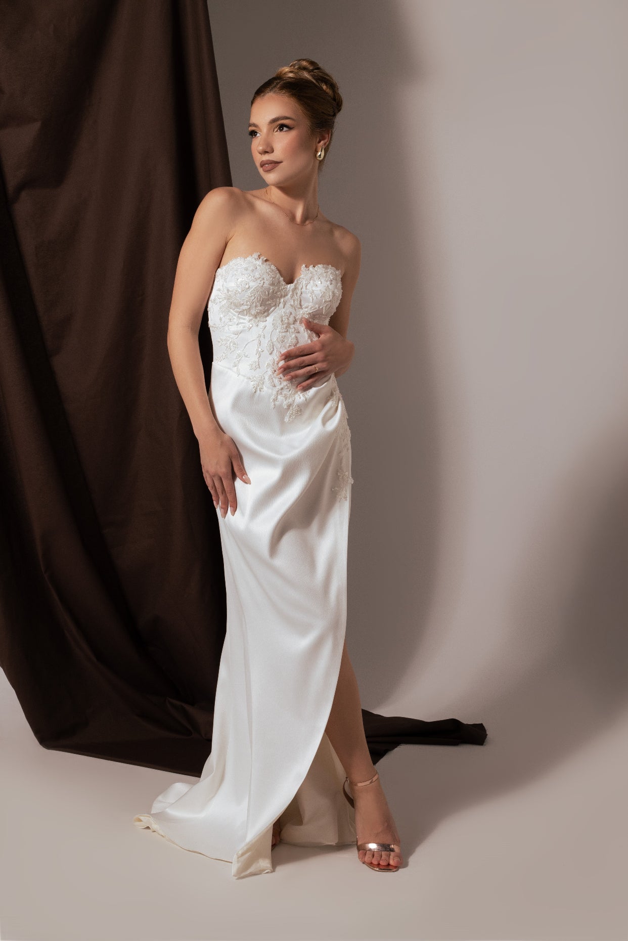 Дълга булчинска рокля Liora LIZA KAIN София. Бяла официална сатенена рокля без презрамки. Срязан корсет с бяла флорална дантела. Права пола с цепка и плохи.