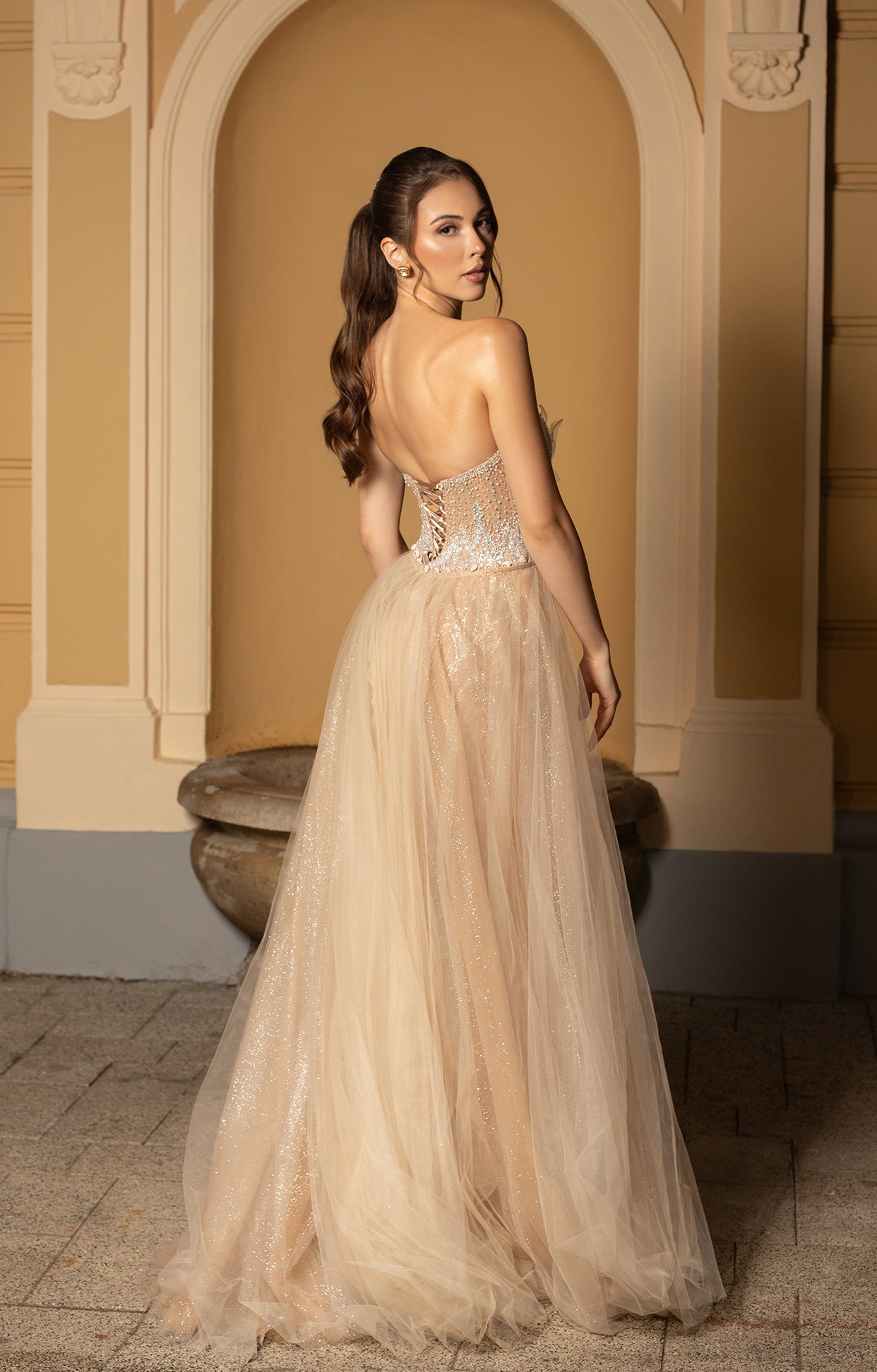 Официална къса абитуриентска рокля Radis LIZA KAIN София. Оформяща кройка с бежова основа, покрита със сребриста дантела от пайети, мъниста и камъчета. Горна част с прозрачни детайли на гърба и талията и връзки. Подвижна обемна бежова пола от тюл. 