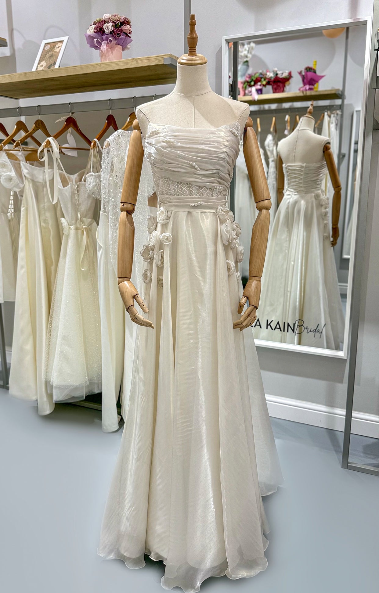 Дълга булчинска рокля Moonblush LIZA KAIN София. Официална бяла рокля от органза. Корсет с дантелена лента и драперия с нашити перли. Свободно падаща пола с тънък колан от органза и апликации от цветя.