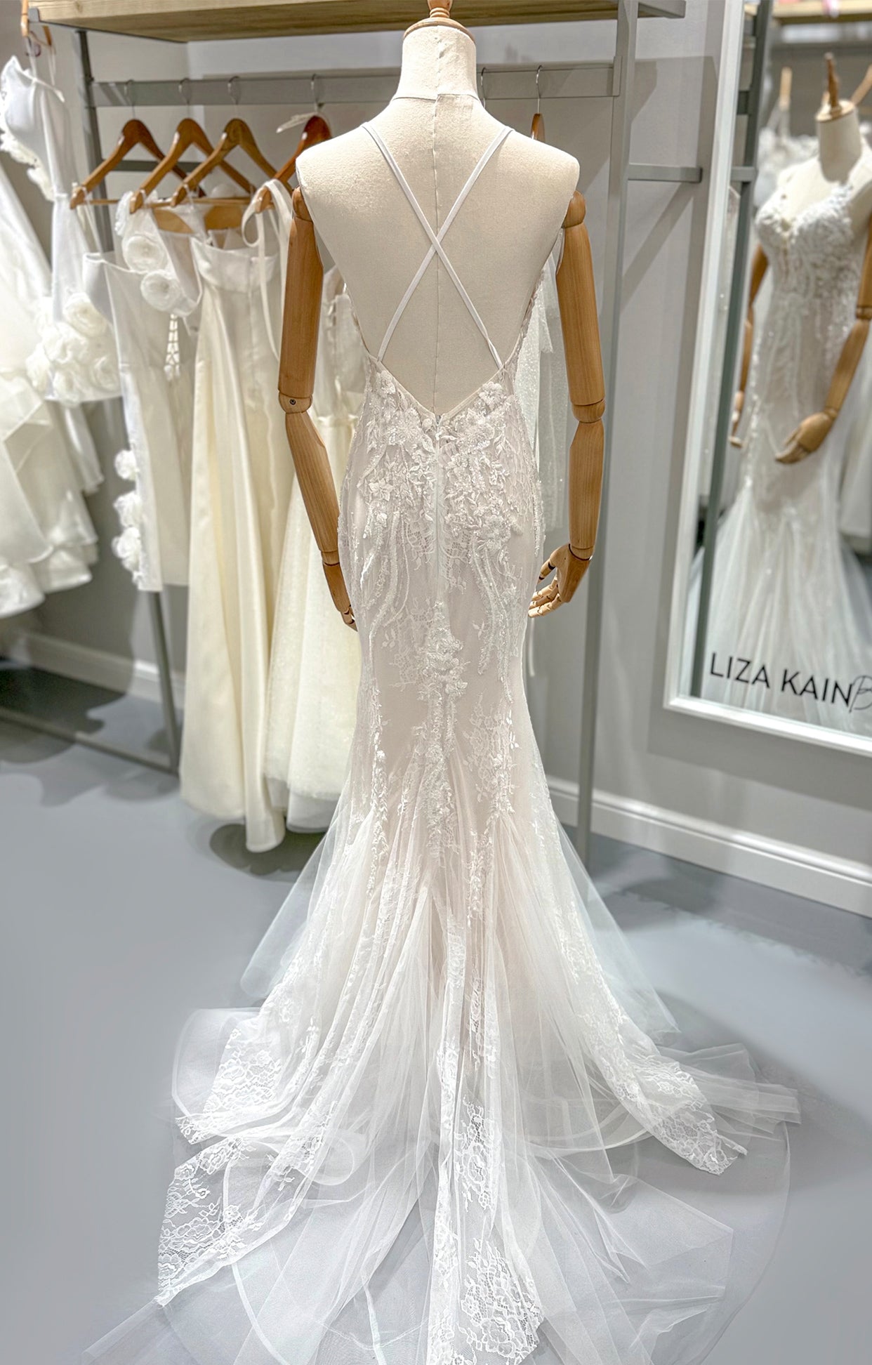 Дълга булчинска рокля русалка Caelina LIZA KAIN София. Официална бяла рокля със силует русалка. V-образно деколте с презрамки X на гърба. Отворен гръб. Флорална дантела. Кройка по тялото. Обемна долна част и шлейф от тюл.