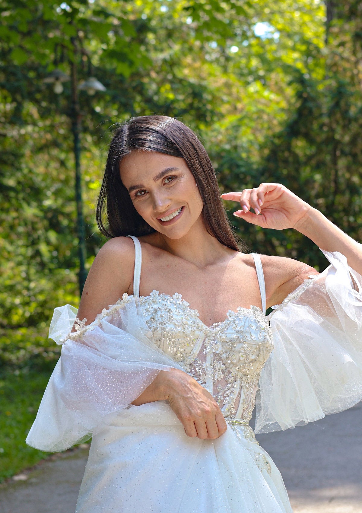 Дълга булчинска рокля Corsseted Bliss LIZA KAIN София. Бяла официална рокля с корсет с чашки и полупрозрачна основа, покрита с блестяща флорална дантела от пайти и мъниста. Презрамки и подвижни тюлени паднали ръкави.