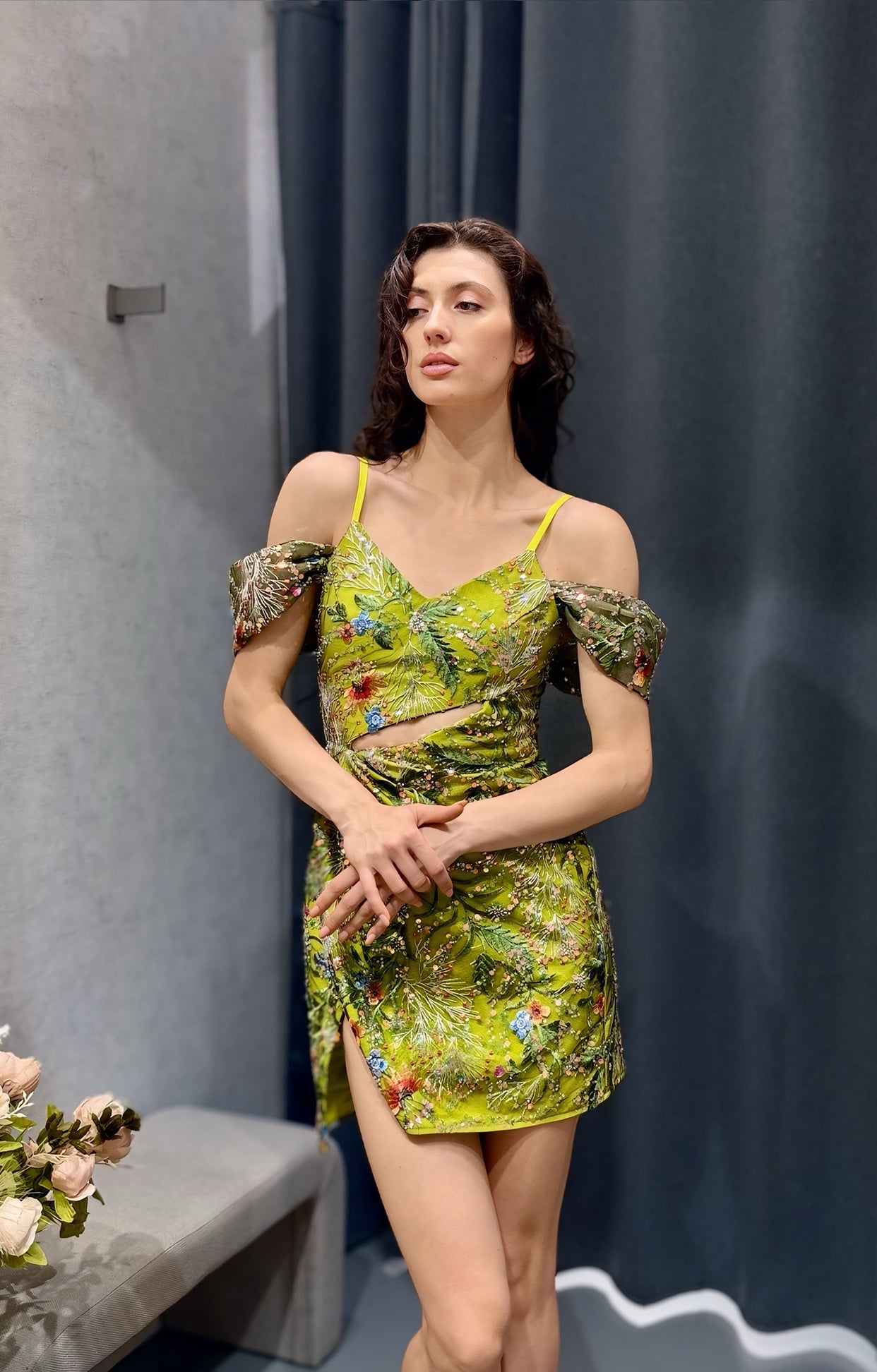 Къса официална рокля Verdant Lace LIZA KAIN София. Зелена коктейлна рокля с презрамки и паднали ръкави. Триъгълно деколте с асиметрично изрязване на талията. Светлозелена основа с многоцветна флорална дантела. Пола по тялото с цепка с прехлупване.