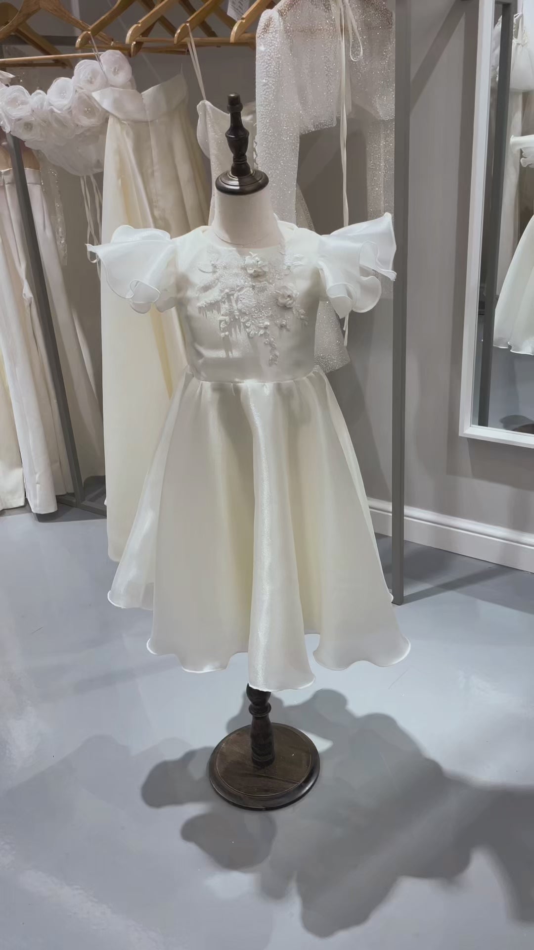 Детска шаферска рокля Amalia. Официална рокля от бяла органза с къси къдрави ръкави. Апликация от памучна флорална дантела. Разкроена пола. Панделка на гърба.