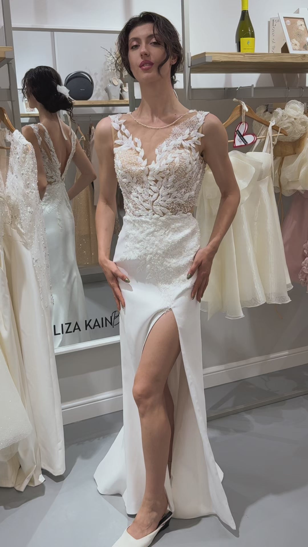 Дълга булчинска рокля Ivy Embrace LIZA KAIN София. Официална бяла рокля с V-образно деколте от дантелени листенца и перли. Отворен V-образен гръб. Сатенена пола по тялото с права цепка и оформящи апликации от дантела. Оформяща кройка.